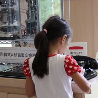 A形自動交換機の黒電話のダイヤルをまわす女の子の後姿の写真