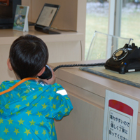 黒電話をかける男の子の後ろ姿の写真