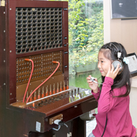 手動交換機の前でヘッドフォンの音を聞く女の子の写真